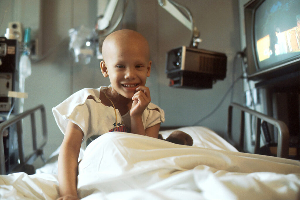 A childhood cancer patient sitting in a hospital bed while receiving treatment