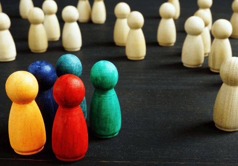 A few multicolored wooden figures surrounded by many white wooden figures, representing systemic inequality