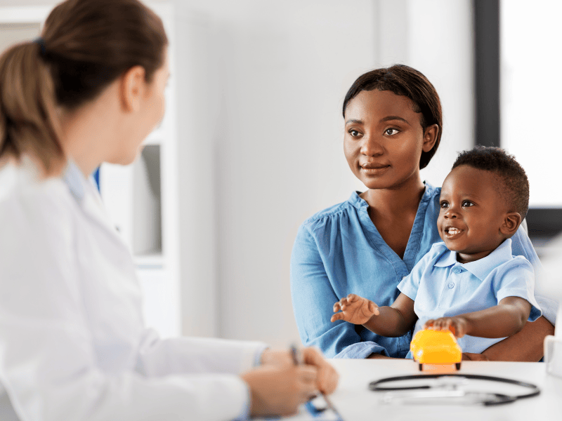 A Black mother and child meeting with a white doctor